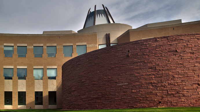 A semi-spherical wall attached to a cylindrical central tower sporting a metal hood atop not unlike an inverted rocket exhaust all flanked by two modest wings of rooms.