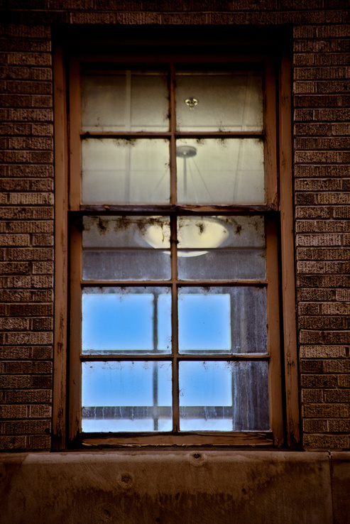 Window with many cobwebs, an interior lit light and blue sky on the other side